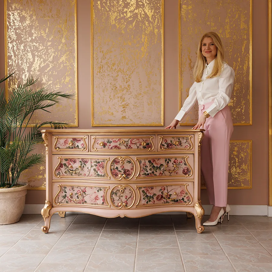 Katarina posing next to a dusty pink French dresser with gold accents and a floral transfer